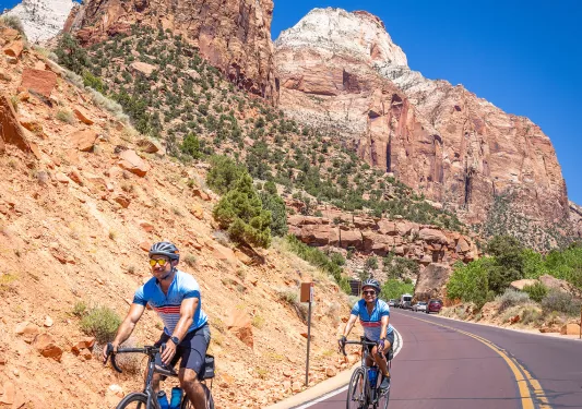 Man and woman biking on an asphalt road with large canyons in the background