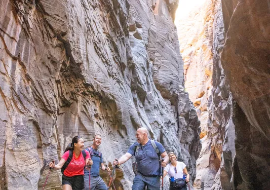 A group of two men and two women walking through a river, in between two canyons
