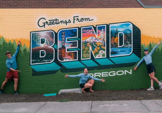 One man and two women in front of a colorful sign of Bend, Oregon