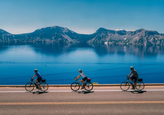 Three people biking on a road next to a large lake