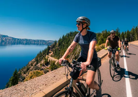 Group of people biking on a road, looking to the left towards a large lake