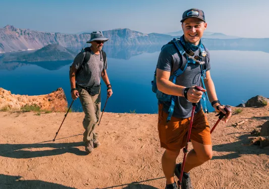 Two men ascending a dirt trail, while using hiking poles