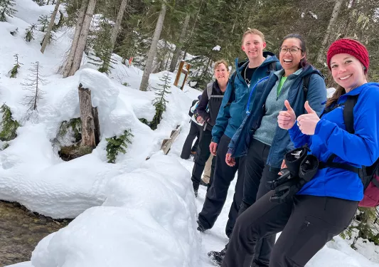 Group of people smiling with two thumbs up, in the middle of a snow patch