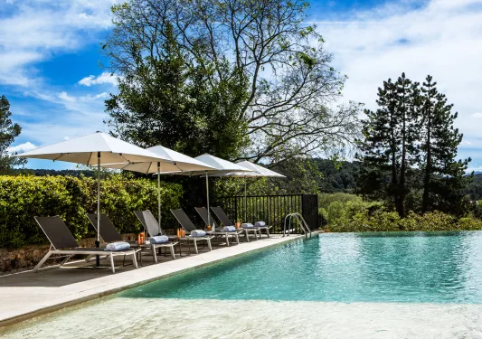 Outdoor pool surrounded by gray, reclining chairs and white umbrellas