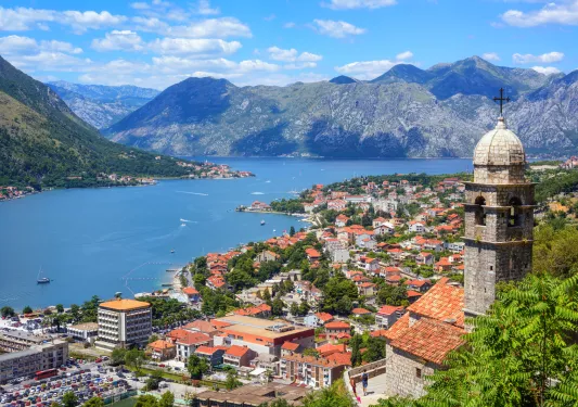 Aerial view of buildings all along the shore of a body of water, mountains in the distance