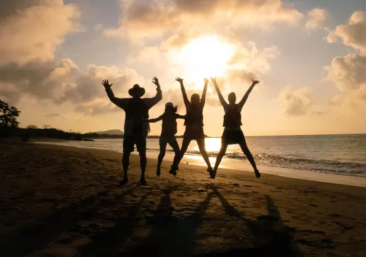 Three peoples silhouettes as they jump against the sunset
