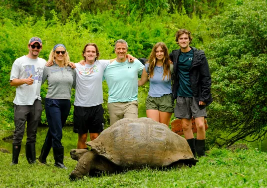 Tourists pose behind a tortoise