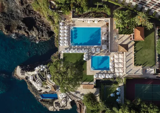 Sky view of outdoor pools with a hotel building next to it