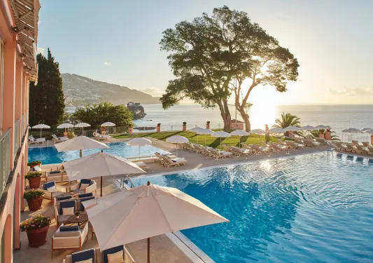 Two outdoor pools with umbrellas and pool chairs along the perimeter