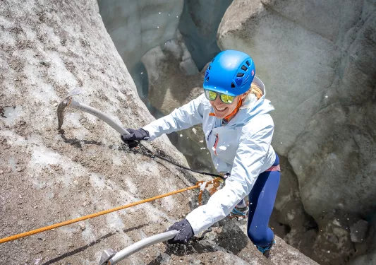 Woman smiling while climbing up a cliff with two sickles