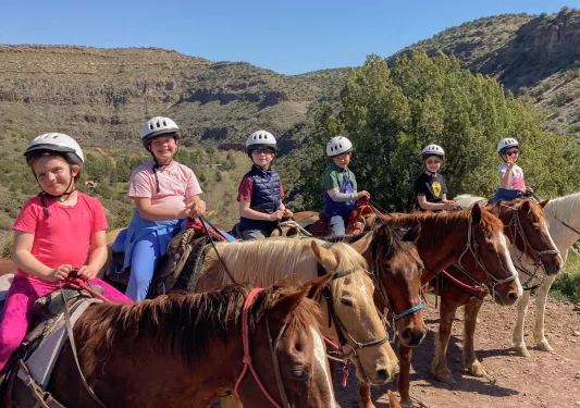Group of kids on horses riding through dirt trails