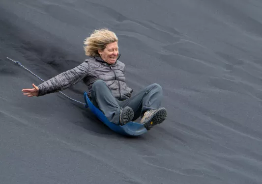Woman sitting on a plastic barrel seat, going down a sandy hill