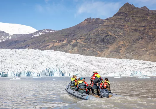 Group of people on a gray raft, going towards snow caps