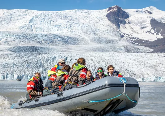 Group of people on a gray raft with snow mountains in the background