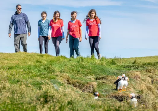 Four women and one man walking on a grassy field