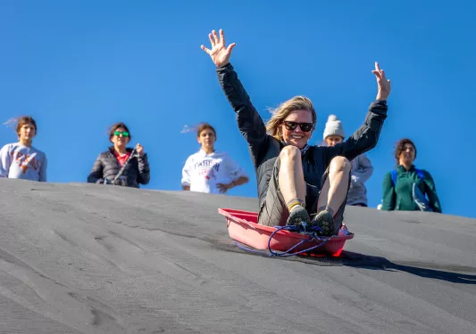 Woman on a red sled, sliding down a sandy hill