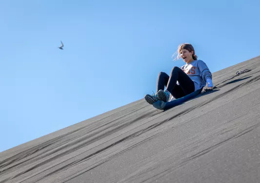 Girl on a plastic sled sliding down a hill of sand