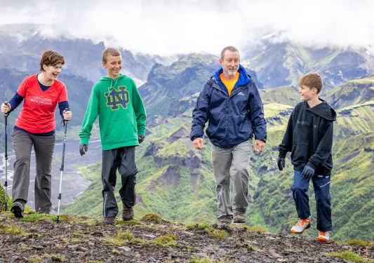Man and women with two kids, walking on a dirt path with fog-covered mountains in the background