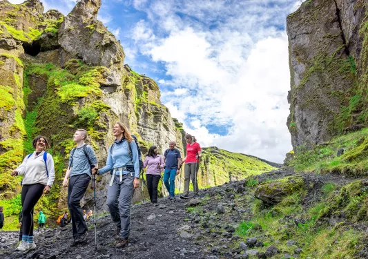 Group of 6 people descending down a dirt and rock trail, with large cliffs on either side of them