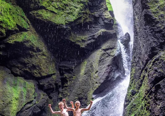 Two boys standing on a rock next to a waterfall