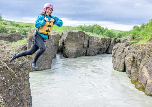 Woman wearing a helmet and life vest jumping into a small lake