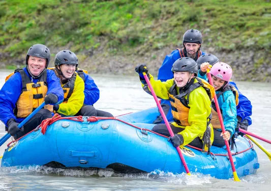 Group of men and women on a blue raft, paddling and smiling