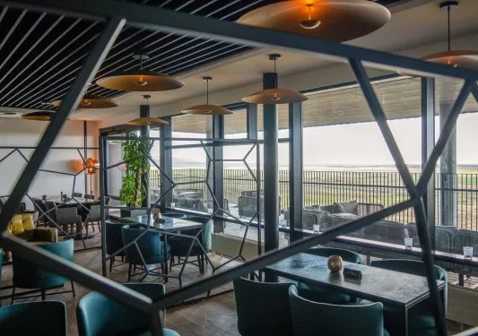 Indoor dining area with stone tables and green, cushioned chairs with large windows
