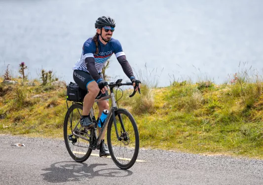 Man riding a bike on an asphalt road with the ocean in the backround