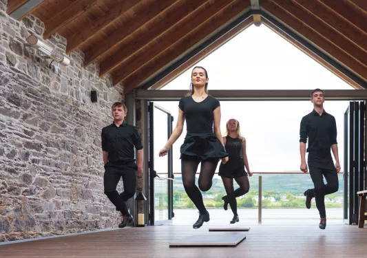 Two men and two women tap dancing in a room with stone walls