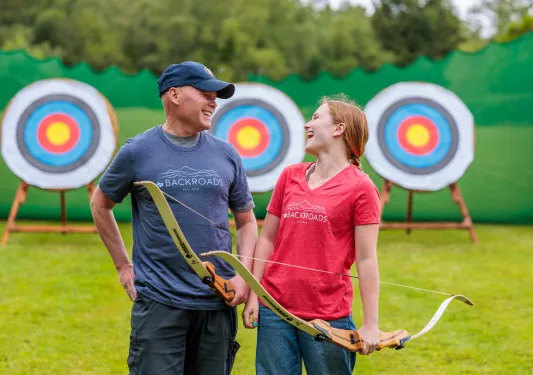 Man and woman smiling at each other while holding archery bows