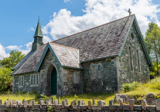 Rustic, stone building surrounded by trees and tall weeds