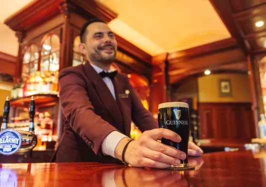 Man with a suit at a bar serving a glass of dark beer