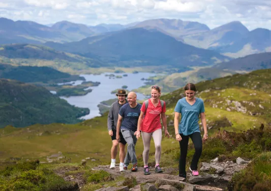 Two men and two women hiking on a stone hill, with a lake in the distance