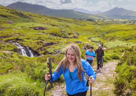Woman with walking poles, ascending a grassy and rocky hill