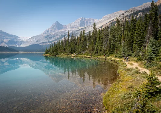 hiking trail next to a clear lake next to mountains