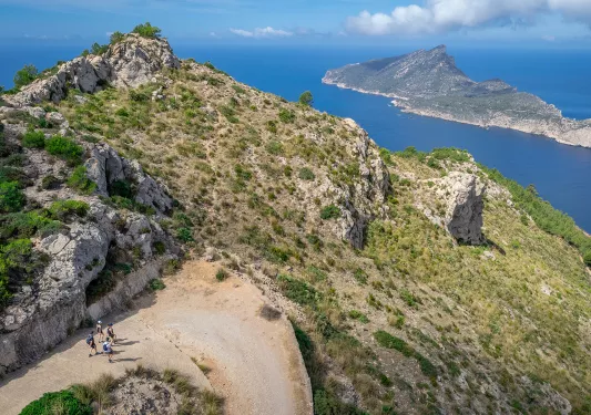 Group of people hiking on a trail along a cliff, with the ocean and an island in the distance