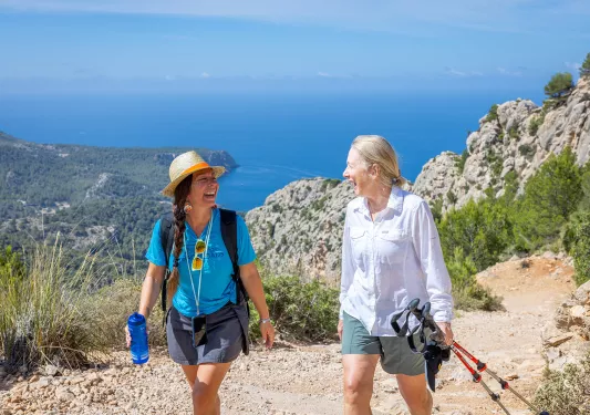 Two women smiling at each other while walking on a dirt trail