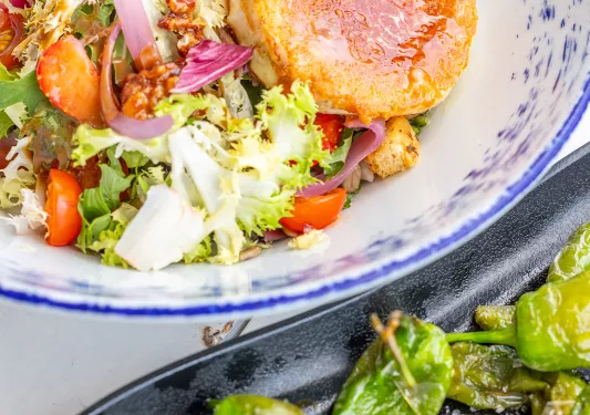 A plate with a salad and another plate with roasted, green peppers