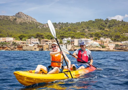 Two men smiling while rowing inside of a kayak in the middle of a lake