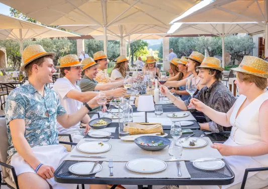 Group of people around a dining table wearing fedoras, while raising their wine glasses