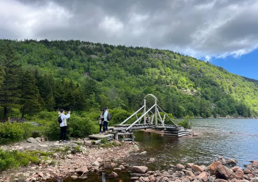 Three women on a wooden bridge by a lake take photos