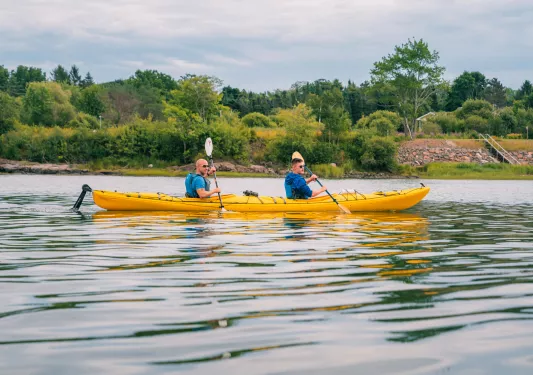 Two men inside of a yellow kayak, paddling in an open lake