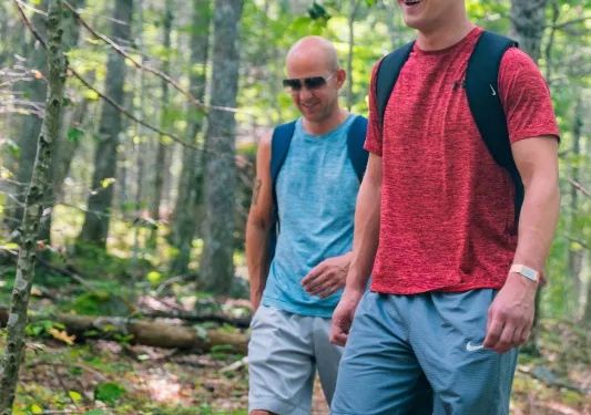 Two men wearing sunglasses hiking through a forest