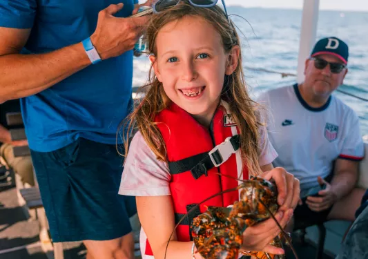 Girl in a red life vest holding up a lobster
