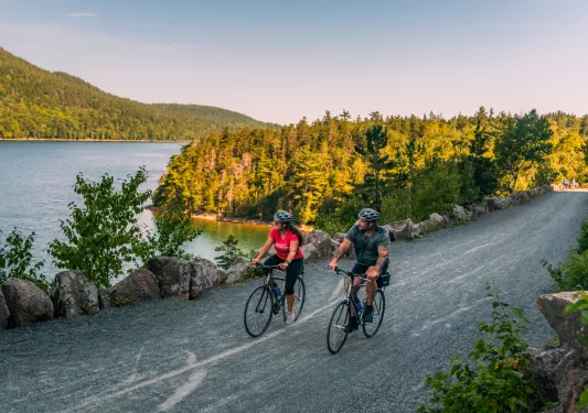 Man and woman riding bikes on a gravel trail next to a lake