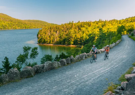 Man and woman riding their bikes on a gravel road next to a lake