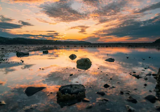 Shallow lake full of larger boulders with the sunset in the background