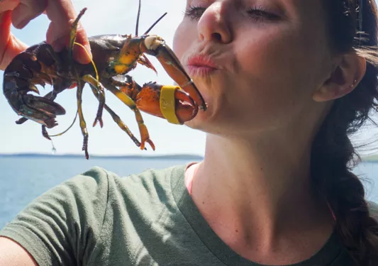 Woman holding up a baby lobster wile puckering her lips