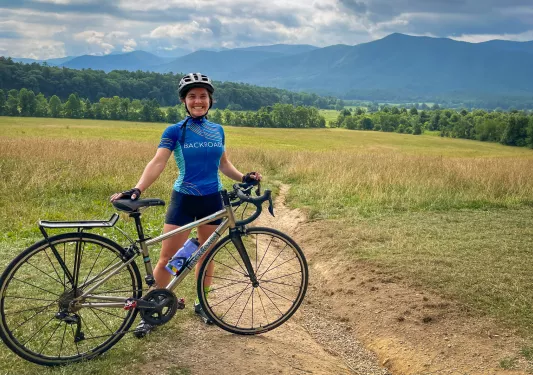 A person with a bike poses in front of a field