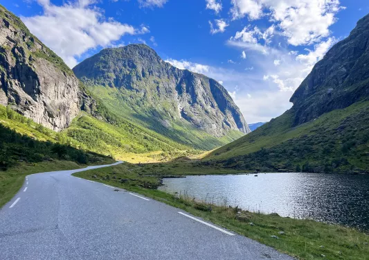 Asphalt road cutting through mountains with a lake to the right